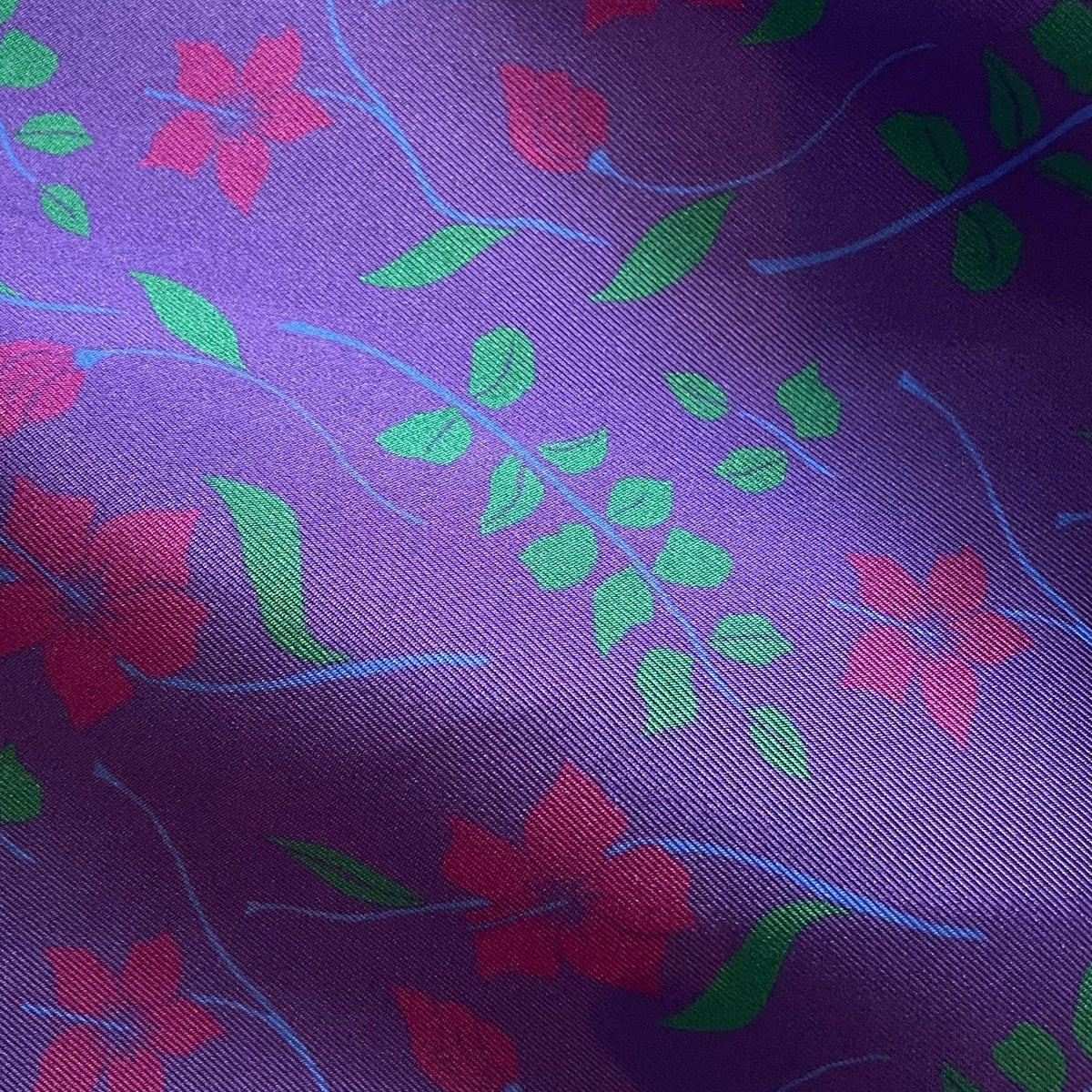 A close-up of the purple hibiscus print silk fabric with a repeating floral pattern in pink and green, accented by thin light blue stems.