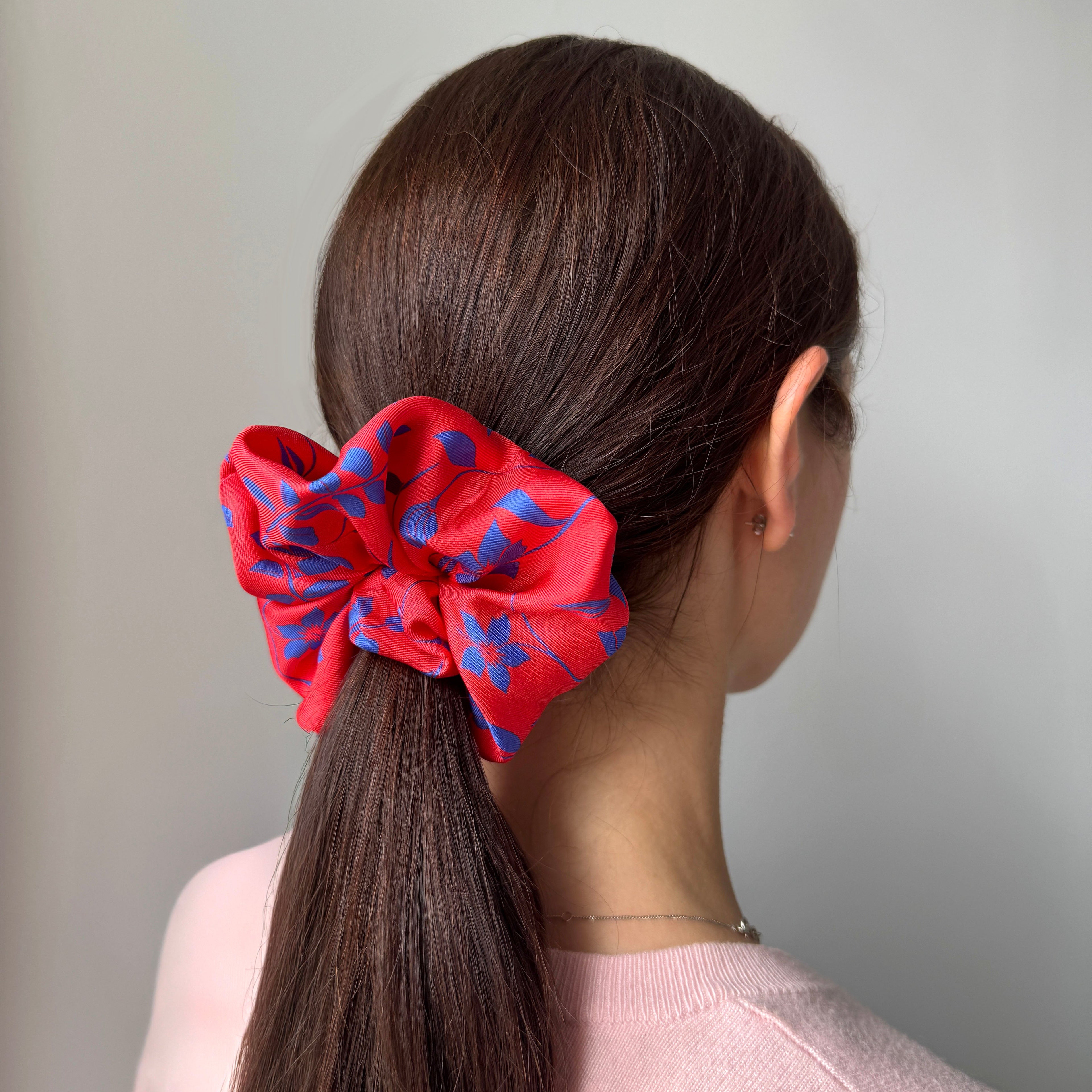 View of woman's head from the back with a bright red and blue floral scrunchie tied in the hair