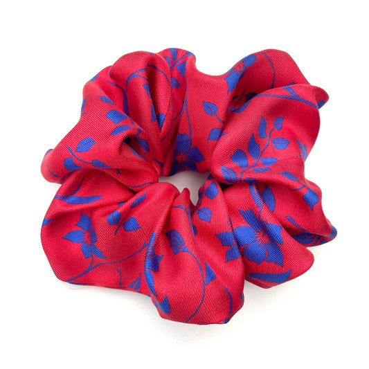 A red fabric hair scrunchie with a blue floral pattern, photographed on a clean white background.